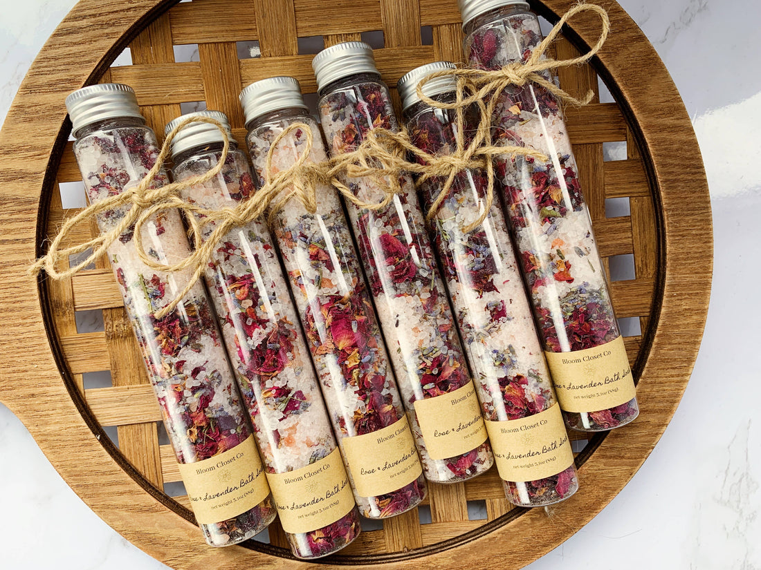 A wooden tray holds five bottles of rose and lavender bath salts in large test tubes.