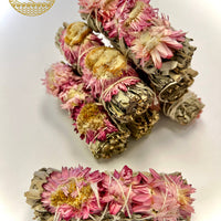Pink sunflowers and white sage bundles elegantly wrapped around a rustic piece of wood.