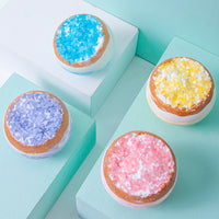 Four colorful sugar balls atop a blue box labeled Essential Oil Bath Himalayan Bath Salt.