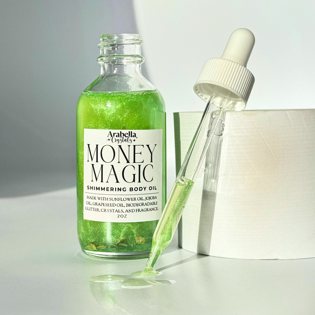 A close-up of Money Magic Shimmer Oil, highlighting its glimmering gold color in an elegant glass bottle.